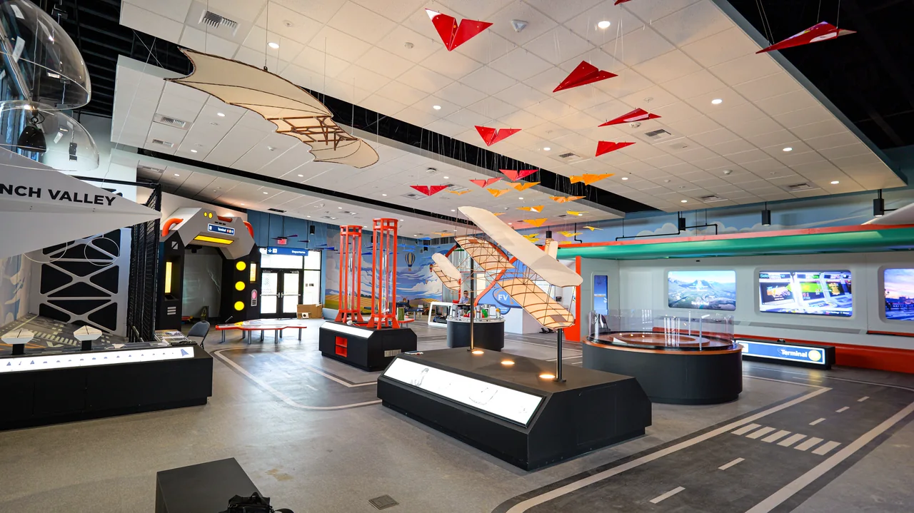 A broad view of the discovery hangar shows exhibits and colorful aircraft overhead.
