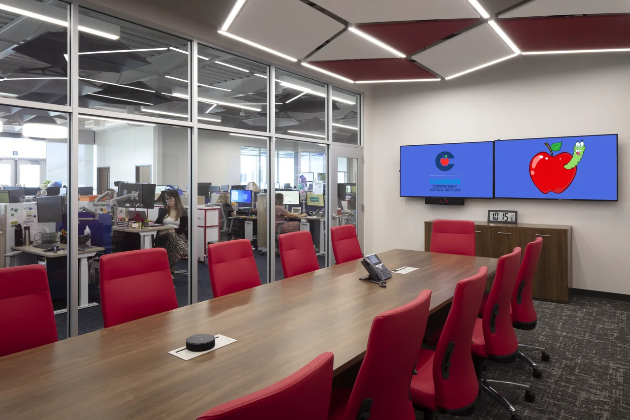 A meeting table stands beside transparent offices in an open collaborative interior.