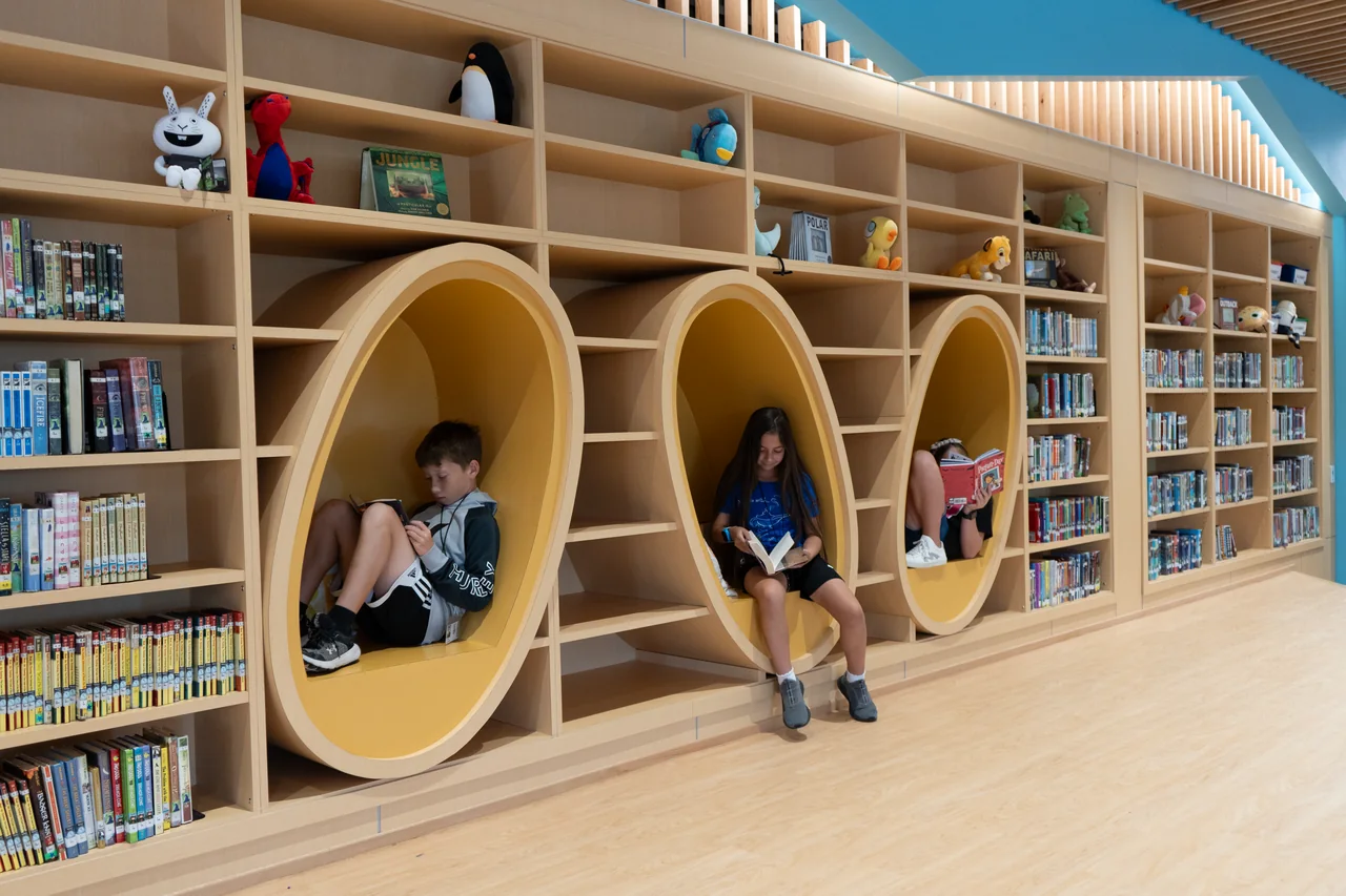 Children reading in circular yellow niches integrated into timber library shelves.