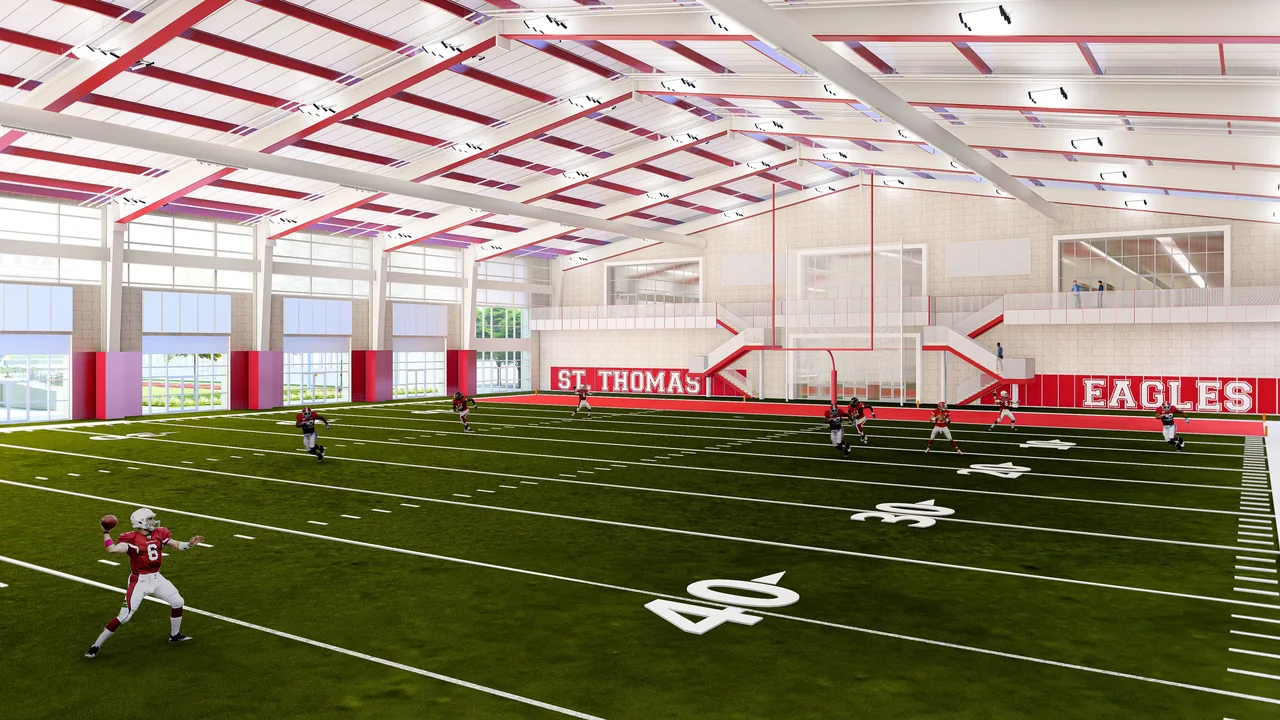 Concept rendering of an indoor football practice field beneath exposed red and white roof framing, with tall windows and an upper-level overlook.